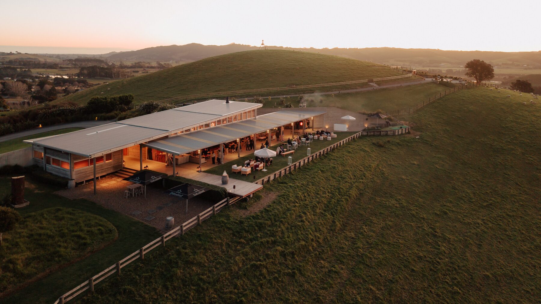 The Lodge at golden hour, guests on the terrace and lawn above the estate's farmland